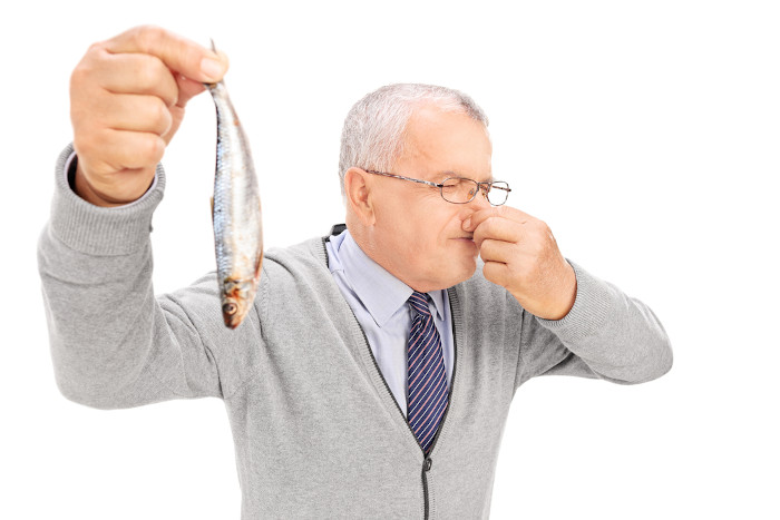 Homem com um peixe na mão e tapando o nariz em referência à amina causadora do odor forte.