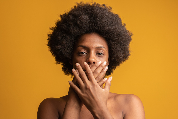 Mulher negra tapando a boca com as mãos em referência ao racismo no Brasil.