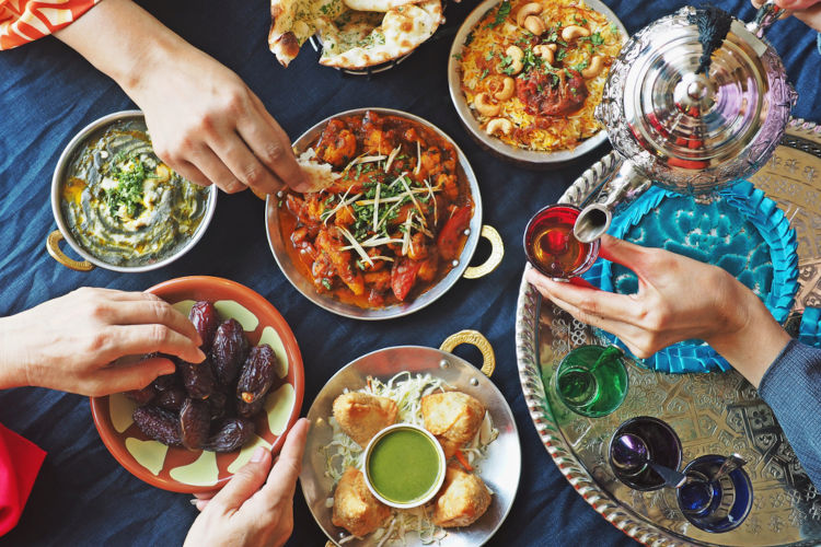 Mãos humanas servindo-se em uma mesa onde há pequenos pratos com alimentos típicos do Iftar, refeição da noite no Ramadã.