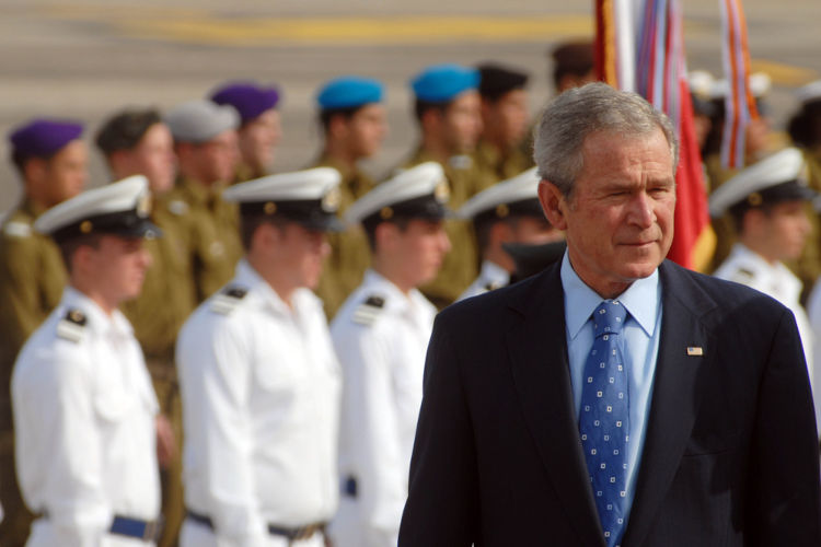 Foto do ex-presidente dos EUA George Bush, em primeiro plano, e, ao fundo, soldados norte-americanos 