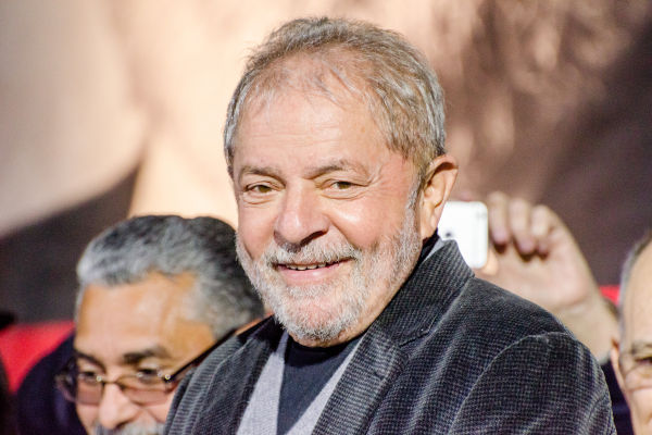 Luiz Inácio Lula da Silva sorrindo cercado de algumas pessoas.