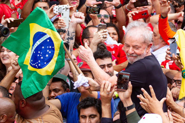 Lula segurando a bandeira do Brasil e sendo carregado por multidão após sua soltura