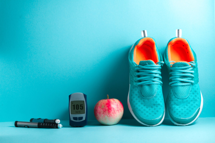 Aparelho medidor de glicemia, uma maçã e um par de tênis de corrida em superfície e fundo azuis
