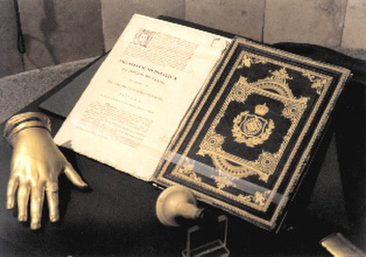 Fotografia da Constituição de 1824; ao lado dela, uma escultura de uma mão dourada