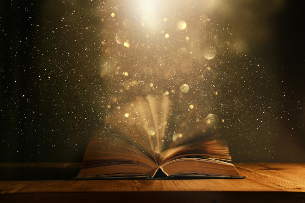 Livro antigo aberto sobre uma mesa de madeira com sobreposição de glitter saindo das páginas com uma ideia de algo mágico.