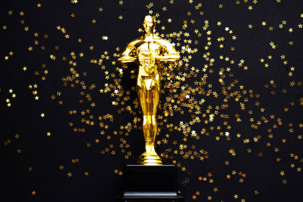 Estatueta dourada do Oscar sobre um fundo preto com estrelas douradas.