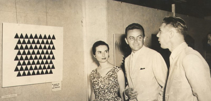 A artista Lygia Pape, em 1957, diante da obra de Luiz Sacilotto e ao lado de dois homens.