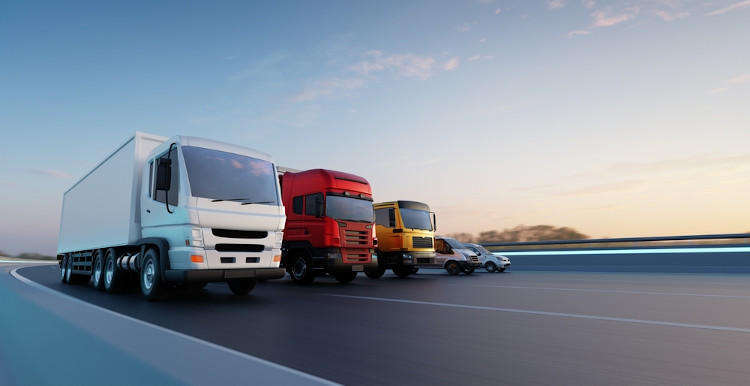Caminhões e carros em estrada exemplificando os tipos de transporte rodoviário.