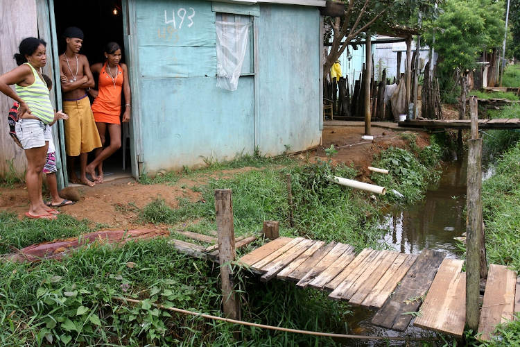 Pessoas em uma moradia próxima a um córrego com águas poluídas, um exemplo da falta de saneamento básico.