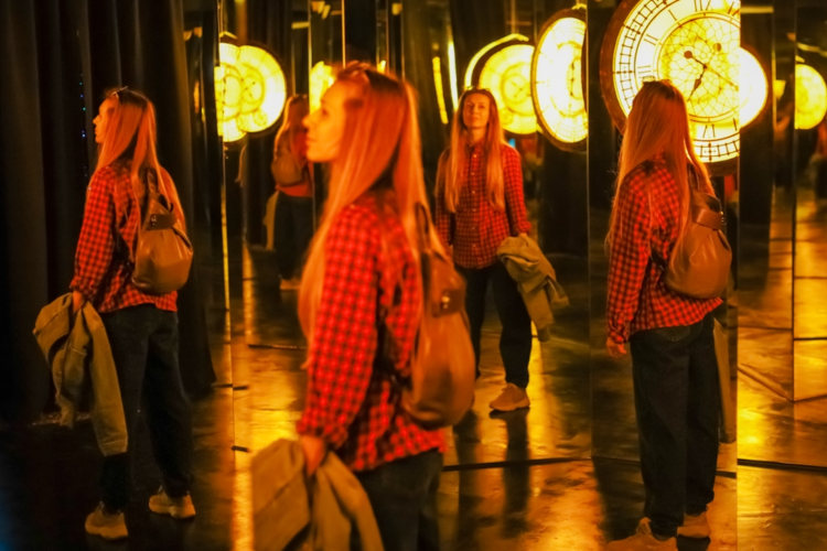 Jovem de camisa xadrez em um labirinto de espelhos planos.