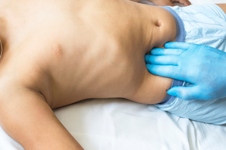 Homem deitado tendo seu abdome examinado pelo toque da mão do médico.