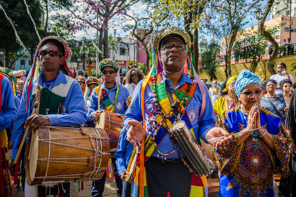 Pessoas caracterizadas com acessórios e instrumentos coloridos em congada realizada em São Paulo. 