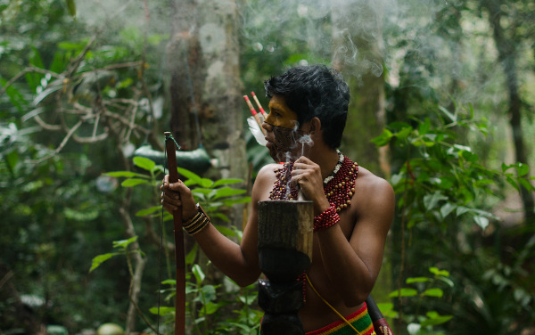 Homem indígena na floresta, com adereços típicos de sua cultura, que é celebrada no Dia dos Povos Indígenas.