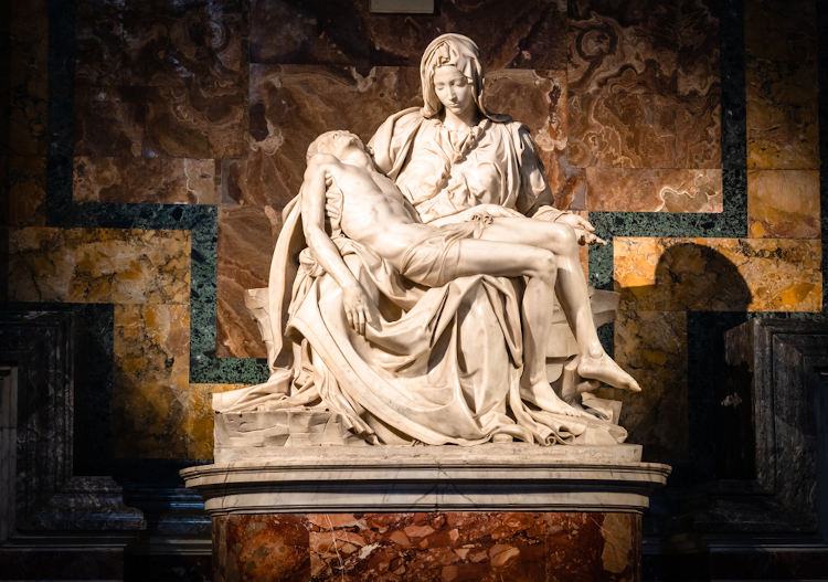 Escultura de uma mulher, que representa a Virgem Maria, segurando em seu colo o corpo morto de Jesus.