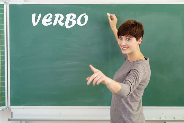 Professora escreve em quadro-negro a palavra “Verbo”.