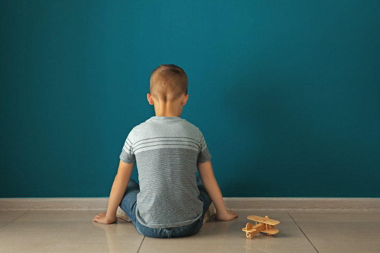 Menino sentado no chão de frente para uma parede, uma alusão ao preconceito contra a pessoa neurodivergente.