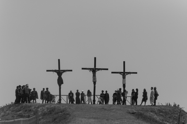 Três homens crucificados no alto de um morro, sendo observados por algumas pessoas; uma encenação comum na Sexta-Feira Santa.