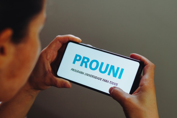 Homem segurando celular com a palavra ProUni na tela.