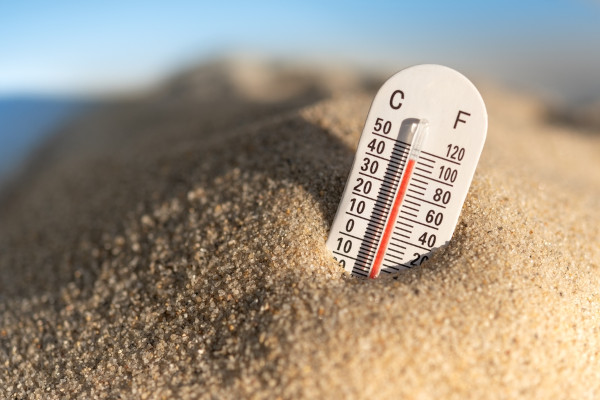 Termômetro com duas escalas termométricas enterrado na areia.