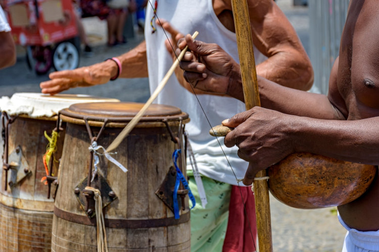 Pessoa tocando berimbau, instrumento musical da cultura brasileira, em uma roda de capoeira.
