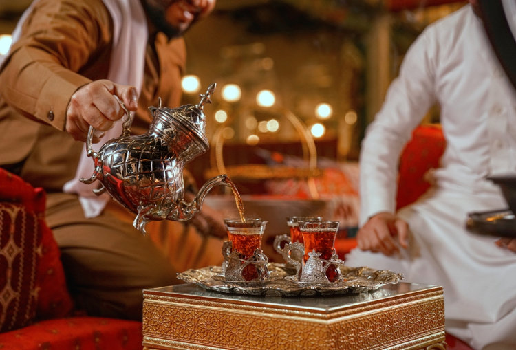 Pessoa servindo o “gahwa” à outra, símbolo de hospitalidade que faz parte da tradição da cultura árabe.