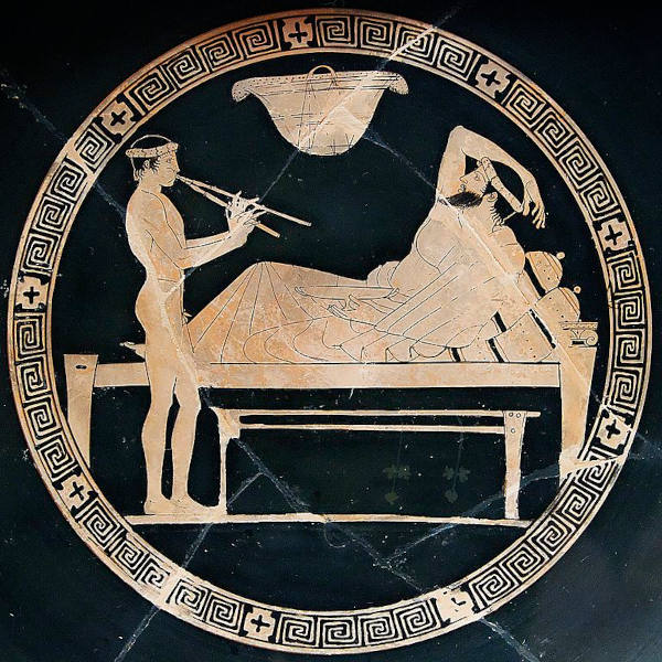 Homem deitado e servo tocando flauta em uma cerâmica grega, em texto sobre a sociedade ateniense. 