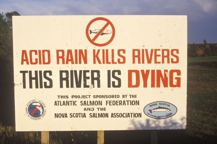 Placa indicando os efeitos nocivos da chuva ácida. Diz, em inglês: “Chuva ácida destrói os rios. Este rio está morrendo”.