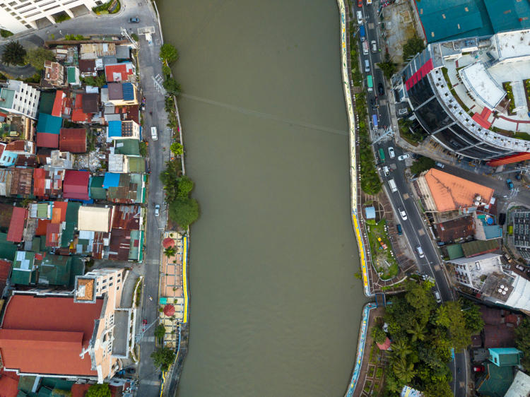 Imagem superior de um rio separando duas cidades no meio urbano, aspecto que pode ter enchentes como consequência.