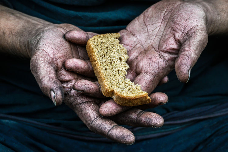 Mãos de uma pessoa em situação de vulnerabilidade segurando um pedaço de pão, uma alusão à fome no mundo.