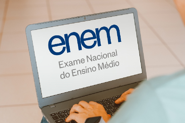 Mulher com as mão sobre o teclado de um notebook que estampa a logo do Enem (Exame Nacional do Ensino Médio).