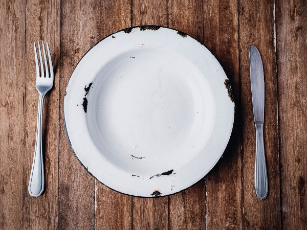 Prato vazio sobre uma mesa de madeira representando a falta de acesso a alimentos, uma das causas da insegurança alimentar.