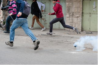 Manifestantes fogem de gás lacrimogênio durante um protesto contra a ocupação israelense na cidade de Hebron, Cisjordânia[1]
